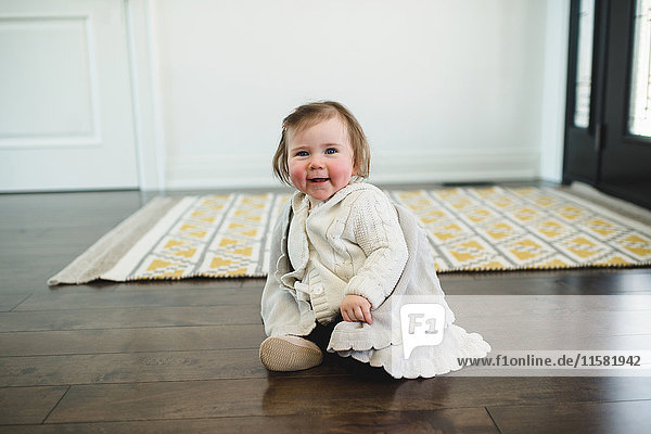 Rosy-cheeked baby sitting on the floor smiling