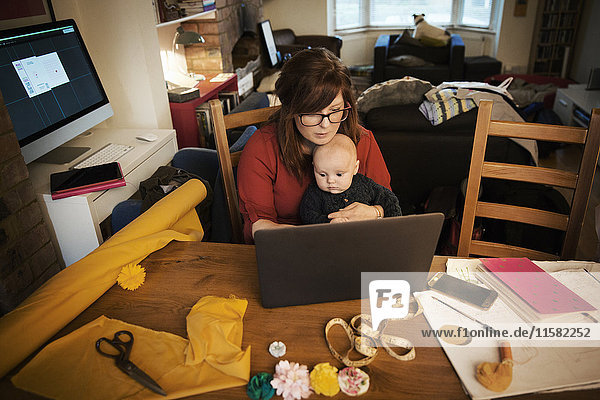 Eine Frau saß mit ihrem Baby auf dem Schoß  Multitasking und mit einem Laptop.