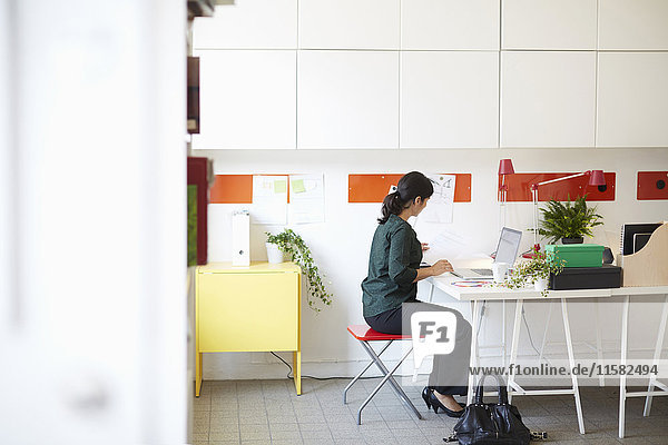 Full length side view of businesswoman with document and laptop at table in office