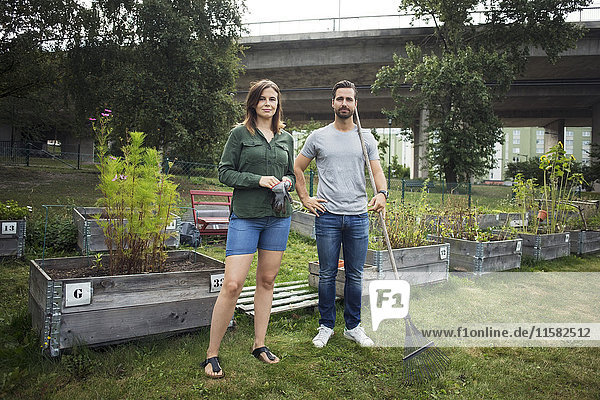 Full length portrait of mid adult couple with gardening tools at urban garden