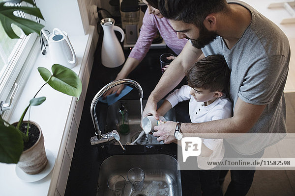 Hochwinkelansicht von Vater und Sohn beim Geschirrspülen durch Frau in der Küche
