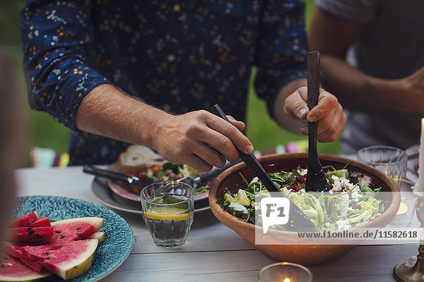 Mittelteil des Mannes beim Mischen von Salat am Tisch während der Gartenparty