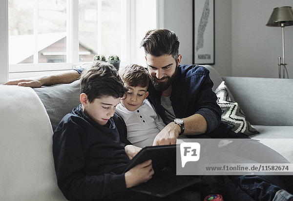 Vater und Söhne beim Sitzen auf dem Sofa zu Hause mit Tablette