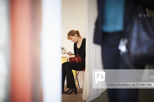 Businesswoman using mobile phone with colleague in foreground at office