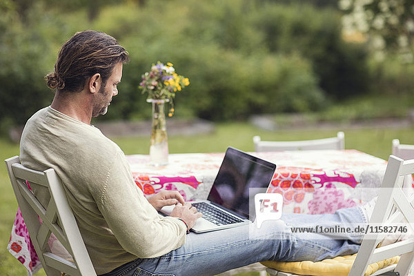 Mann  der den Laptop benutzt  während er auf einem Stuhl im Hinterhof sitzt