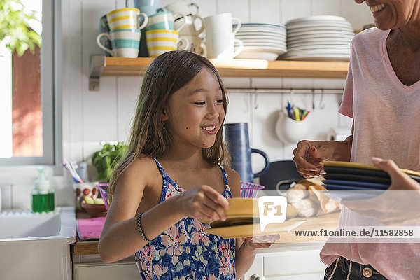 Happy girl holding plates with mother in kitchen at home