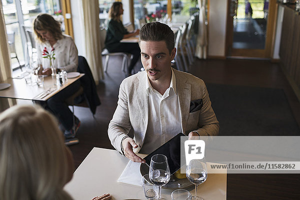 Geschäftsmann im Gespräch mit einer Kollegin bei der Präsentation des digitalen Tabletts im Restaurant