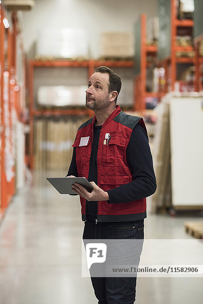 Salesman holding digital tablet while looking at shelf in hardware store