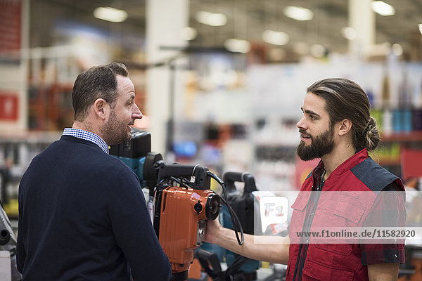 Verkäufer im Gespräch über Maschinen mit männlichen Kunden im Baumarkt