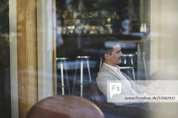 Side view of confident businessman sitting in restaurant seen from window