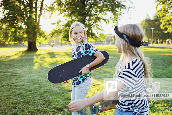 Lächelnde Freunde mit Skateboards  die auf dem Grasfeld spazieren gehen