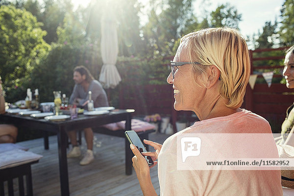 Rückansicht der glücklichen Frau mit Handy im Hinterhof bei Sonnenschein