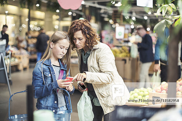 Mutter und Tochter mit Smartphone im Bioladen