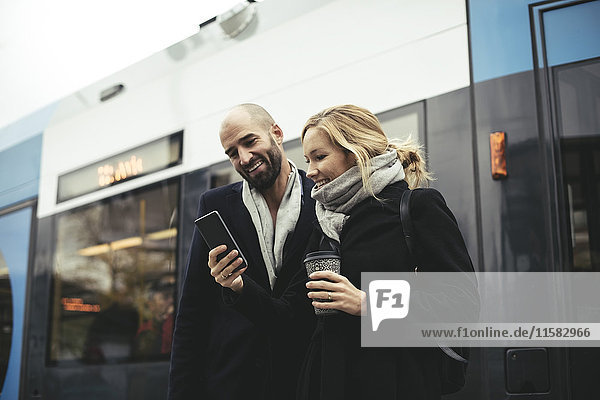 Lächelnde Geschäftsleute mit dem Handy gegen die Straßenbahn