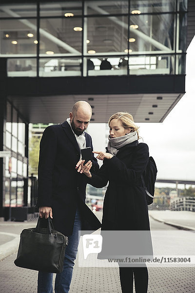 Businesswoman showing smart phone to businessman on city street