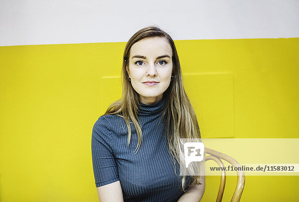 Porträt einer selbstbewussten jungen Frau  die im Büro an der gelben Wand sitzt.