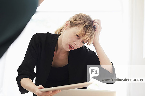 Verwirrte Geschäftsfrau kratzt den Kopf  während sie ein digitales Tablett im Büro benutzt.