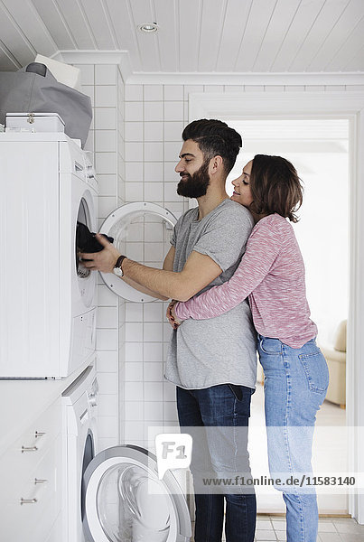 Frau umarmt den Mann beim Beladen der Wäsche in der Waschmaschine zu Hause