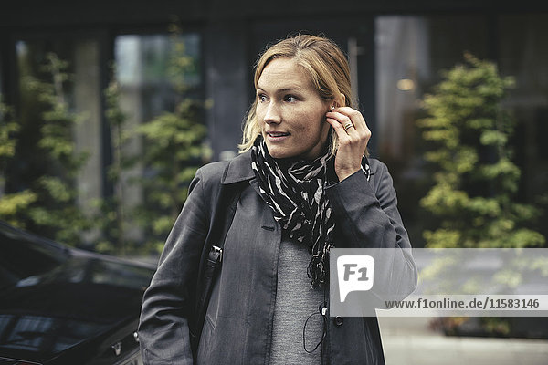 Mittlere erwachsene Geschäftsfrau mit Kopfhörern beim Überqueren der Straße