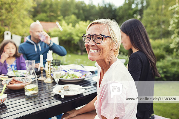 Glückliche Frau sitzt mit Freunden und Familie am Esstisch im Garten während der Gartenparty.