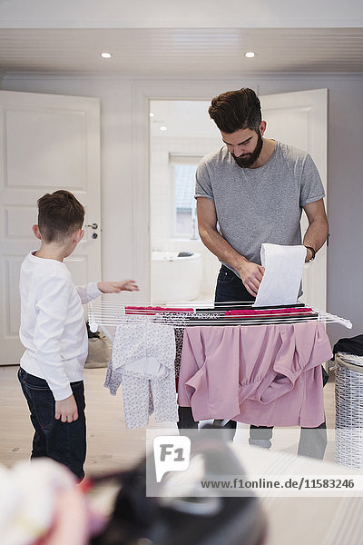 Junge steht neben Vater und trocknet die Wäsche zu Hause.
