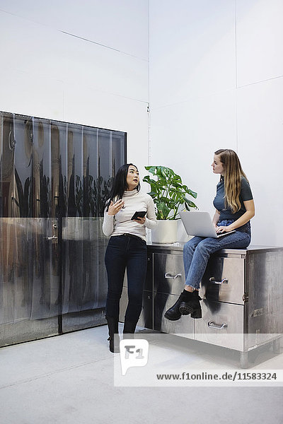 Weibliche Blogger sprechen  während sie Technologien im kreativen Büro nutzen.