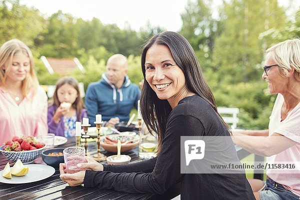 Porträt einer Frau  die mit Freunden und Familie bei einer Gartenparty am Tisch sitzt.