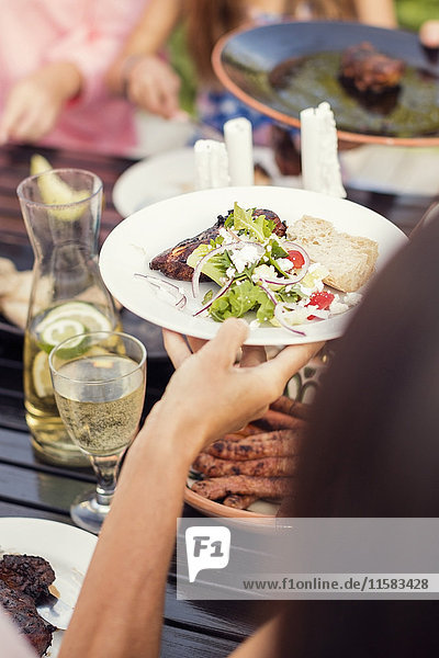 Cropped hand of woman holding food plate over dining table in back yard