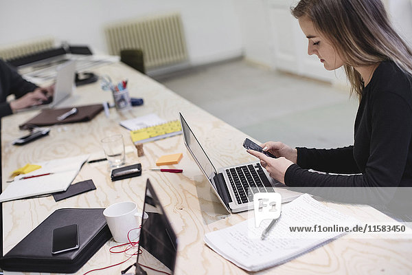 Young woman using smart phone at desk in creative office