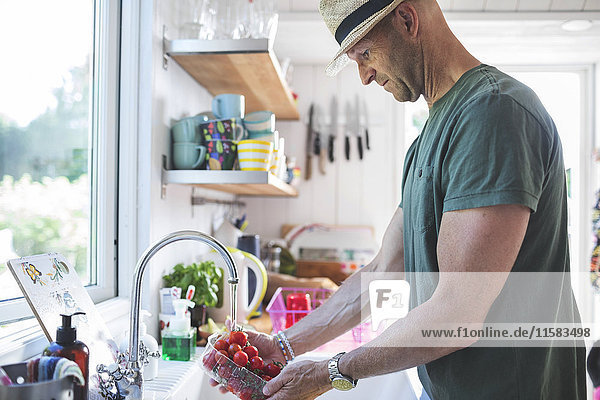 Side view of man washing cherry tomatoes under faucet in kitchen at home