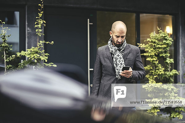 Mid Erwachsenen Geschäftsmann mit Smartphone gegen Gebäude