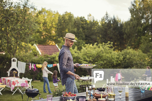 Mann mit Teller beim Esstisch im Garten während der Gartenparty