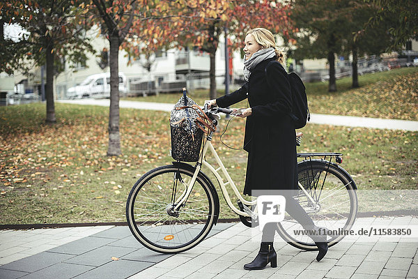 Durchgehende Seitenansicht der Geschäftsfrau mit Radwanderung auf dem Fußweg im Herbst