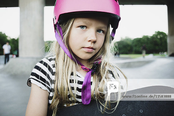Portrait of girl wearing pink helmet holding skateboard at park