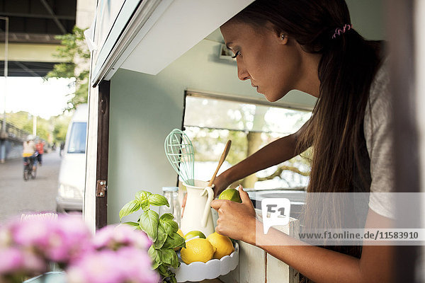 Side view of female owner holding lemon while working in food truck