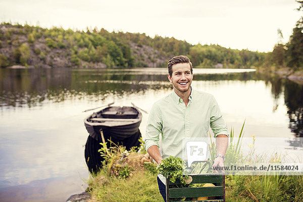 Lächelnder Mann mit Gemüsekiste beim Stehen am See