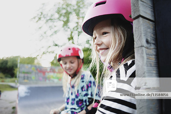Lächelndes Mädchen mit Helm sitzend mit Freund am Rand der Skateboard-Rampe