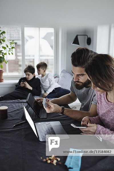 Mother and father shopping online with sons in living room at home