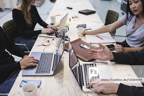 Beschnittenes Bild von vier Personen  die den Laptop am Schreibtisch im Büro benutzen