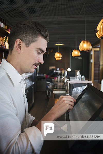 Side view of owner using cash register at checkout in restaurant