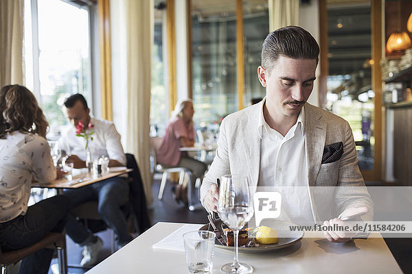 Businessman eating lunch while using smart phone at restaurant