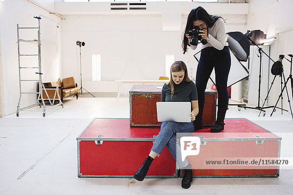 Blogger photographing female colleague using laptop in creative office