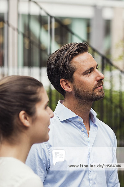Mid adult businessman and businesswoman looking away while standing at office yard