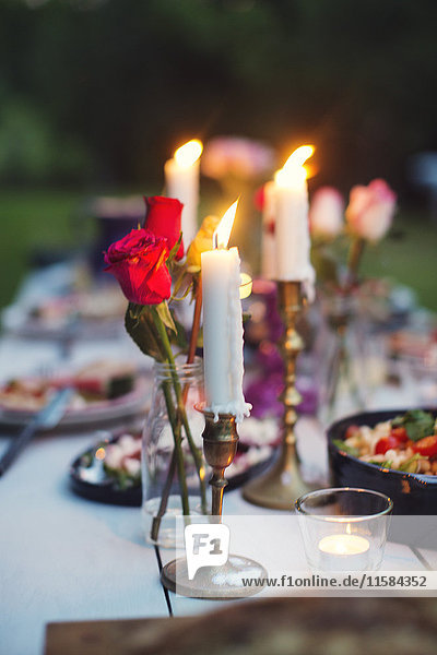 Rosen in Vase und angezündete Kerzen inmitten des Essens auf dem Tisch bei der Gartenparty