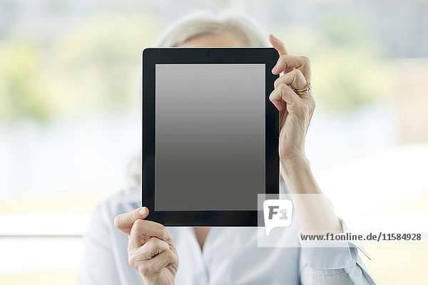 Frau hält digitales Tablet vor ihr Gesicht.