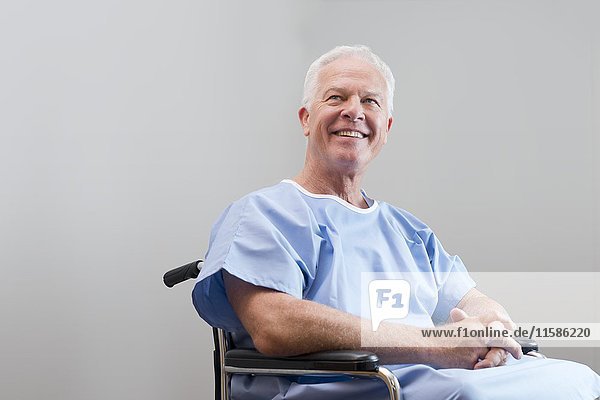 Senior man in hospital gown in wheelchair  smiling.