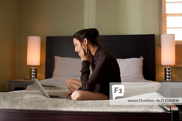 Woman sitting on bed using laptop