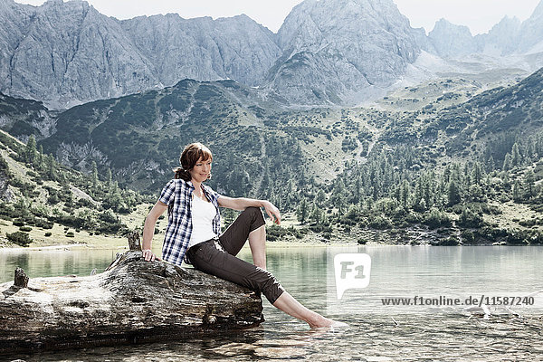 Frau baumelt mit den Füßen im See