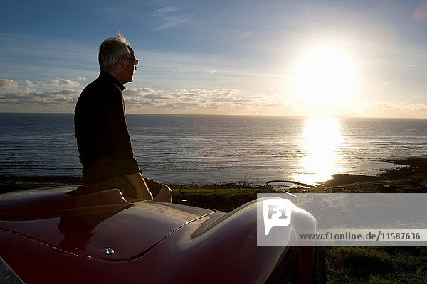 Älterer Mann betrachtet Sonnenuntergang von der Motorhaube