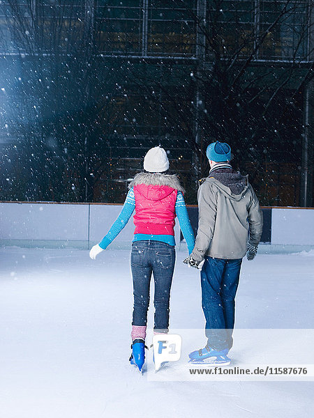 Couple holding hands on the ice rink watching the snow falling